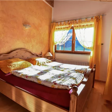 A cozy bedroom with a large bed and colorful bedding. Bright curtains let in plenty of daylight.