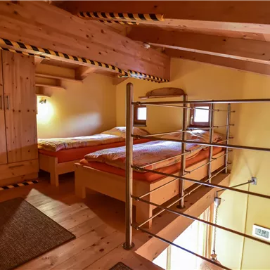 A cozy room with wood paneling and two beds. The facade is light yellow, and there is a modern railing on the upper floor.