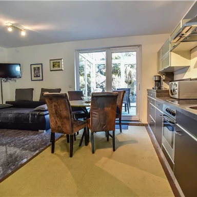 A modern kitchen with a dining area and a living room. Large windows offer a view of the garden.