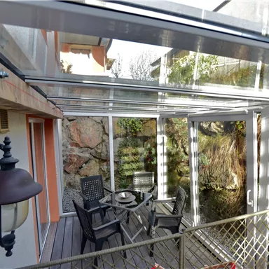 A cozy conservatory with a table and chairs. Large windows offer a view of the nature outside.