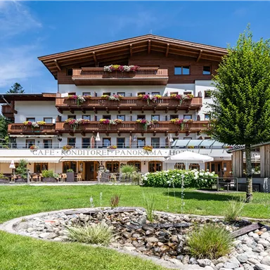 A charming guesthouse in a picturesque landscape with colorful flower boxes. The terrace invites you to relax outdoors, surrounded by green meadows and mountains in the background.