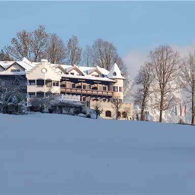 Ein verschneites Hotel in einer ruhigen Winterlandschaft. Die Bäume und das Gebäude sind von frischem Schnee bedeckt.