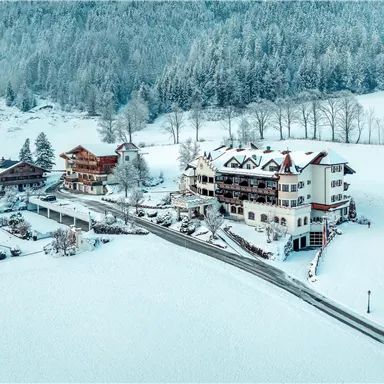 Eine winterliche Landschaft mit schneebedeckten Häusern und hohen Bäumen. Die Umgebung ist ruhig und verschneit, ideal für einen idyllischen Rückzugsort.