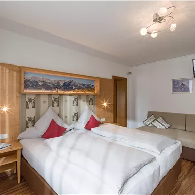 A modern hotel room with a double bed and wooden paneling. A television hangs on the wall and there is a cozy seating area.