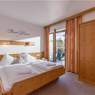 A cozy bedroom with two beds, wood paneling, and a balcony. Large windows let in plenty of light and offer a view outside.