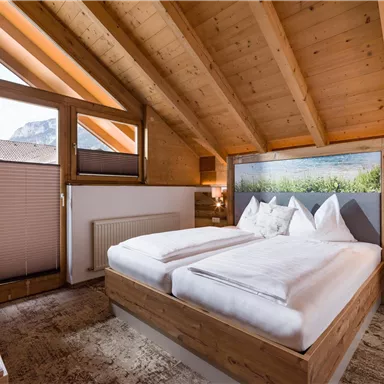 A cozy bedroom with wooden walls and a skylight. It is decorated with a double bed and a beautiful landscape painting.