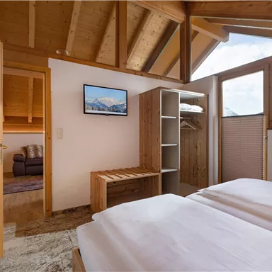 A cozy bedroom with two single beds and wooden furniture. The room has large windows with a view of the mountains and a comfortable seating area.