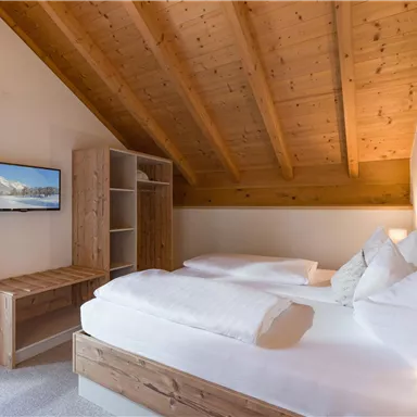 A cozy bedroom with two beds and a wooden ceiling. The room is bright, with a television and a small wooden desk.