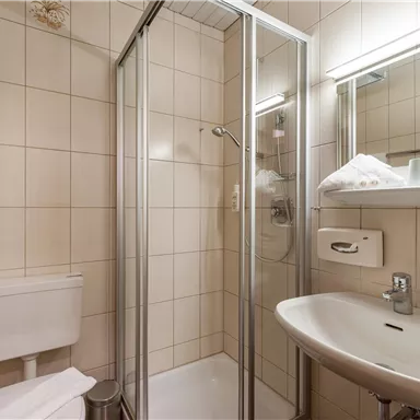 A modern bathroom with a shower cubicle and a sink. There are bright tiles and some towels on a shelf.