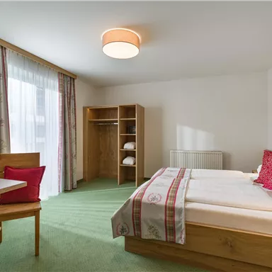 A bright hotel room with a double bed, a table and chairs. Large windows let in plenty of light and there is a wardrobe.