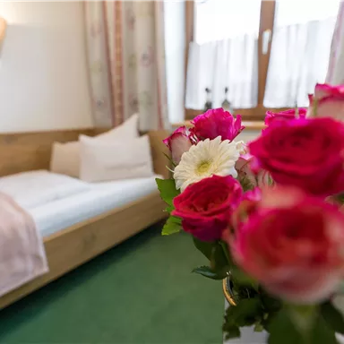 A cozy room with a bed and a beautiful flower arrangement in the foreground. The atmosphere feels inviting and friendly.