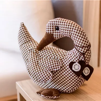 A cozy stuffed duck figure sits on a table. It has a brown-and-white pattern and a sweet expression.