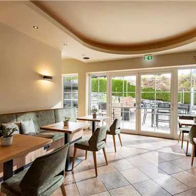 A cozy café with wooden tables and green chairs. Large windows offer a view of the outdoor area.
