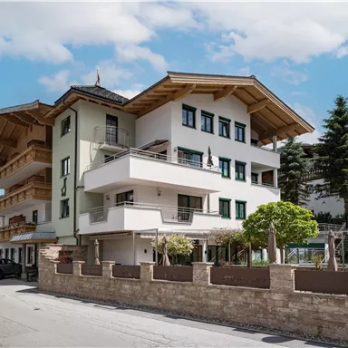 A modern building in alpine style with wooden elements. It is located on a road, surrounded by trees and beautiful scenery.