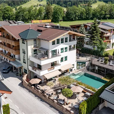 A modern hotel with several buildings and a swimming pool. The surroundings are green and offer a picturesque view.