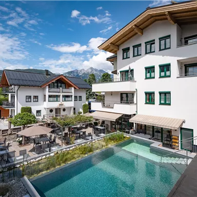 A modern hotel with a beautiful outdoor area and a pool. In the background, green meadows and mountains can be seen.