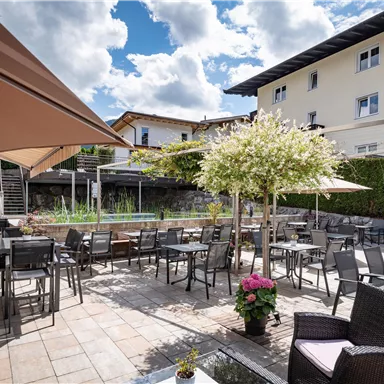 An inviting terrace with tables and chairs under sun umbrellas. Surrounded by plants and a clear sky.