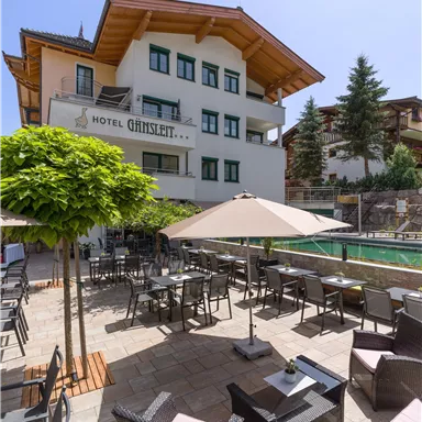 An elegant hotel with a beautiful outdoor area and comfortable furniture. The terrace is decorated with sun umbrellas and plants.