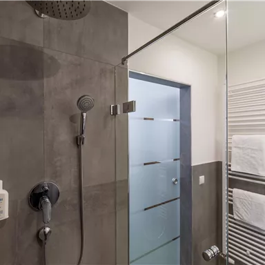 A modern shower with gray walls and a glass partition. Towels are neatly placed on a towel rack.