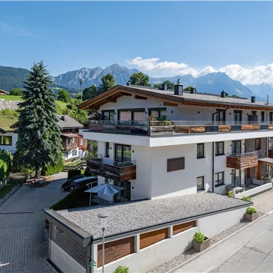 A modern building in a beautiful landscape with mountains in the background. The street in front of the house is quiet and lined with trees.