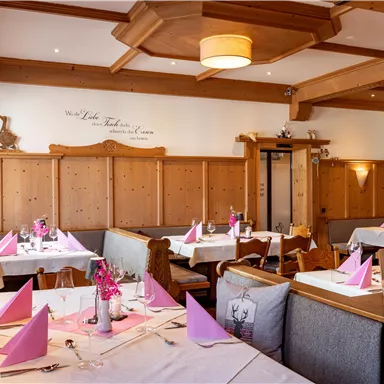 A cozy restaurant with wooden paneling and decorative elements. The tables are nicely set with pink napkins and fresh flowers.