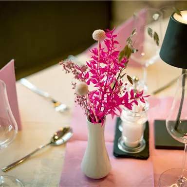 A stylishly laid table with a pink flower vase and elegant glasses. The atmosphere is accentuated by a small lamp and decorative elements.