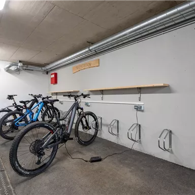 A modern bicycle storage room with several e-bikes and charging connections. The walls are plain and uninviting, which leaves a clean impression.