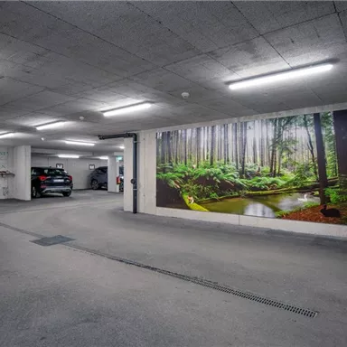 A modern underground garage with a large mural of a forest. In the background, several vehicles are parked, and bicycles are stored.