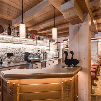 A cozy bar with wooden elements and elegant lighting. In the background, drinks and seating options are visible.