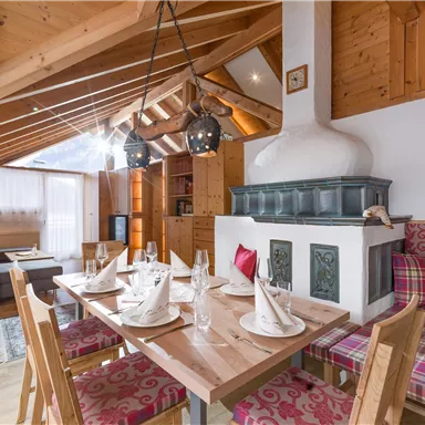 A cozy living room with a dining table, wooden ceiling, and traditional fireplace. The decor is rustic and inviting.