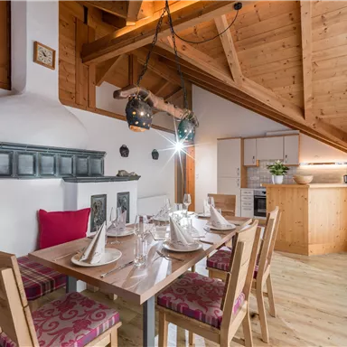 A modern dining room with a large table and cozy chairs. The wooden beam ceiling and the stylish interior design give the room an inviting atmosphere.