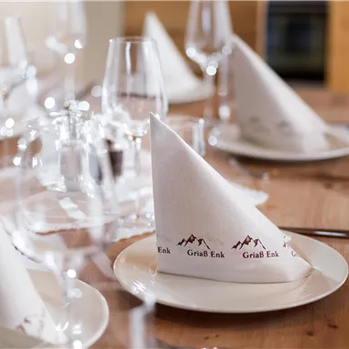 A beautifully set table with white napkins and glasses. The napkins are elegantly folded and adorned with a logo.