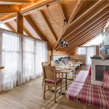 A cozy room with a wooden ceiling and large windows. There is a dining area with tables and chairs as well as a relaxed seating area.