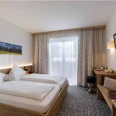 A cozy hotel room with two beds and modern design. It features a desk and large windows that provide plenty of daylight.