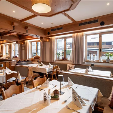 A cozy restaurant with wooden decor and tablecloths. The windows let in a lot of light and offer a view outside.