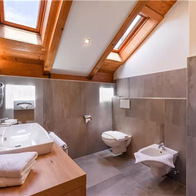 A modern bathroom with wooden ceilings and large windows. It includes a bathtub, a toilet, and elegant fixtures.