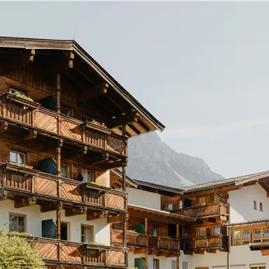 A charming building in alpine style with balconies and wooden cladding. In the background, mountains can be seen, providing a picturesque landscape.