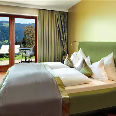An elegant bedroom with a large bed and cozy decor. The windows offer a beautiful view of the green countryside and a terrace.