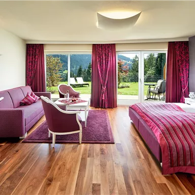 A modern hotel room with purple colored curtains and furniture. Large windows offer a view of the green landscape.