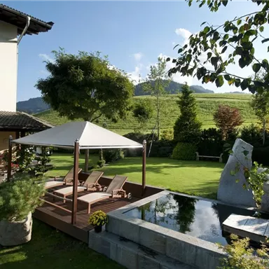 A beautiful garden with sun protection and comfortable loungers. In the background, gentle hills and lush greenery can be seen.
