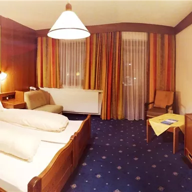 A cozy hotel room with two beds and a desk. The walls are painted in warm colors, and there is a television as well as a window with curtains.