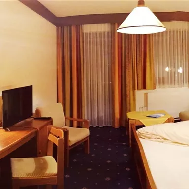 A cozy hotel room with a double bed and a seating area. The room has warm lighting and a friendly atmosphere.