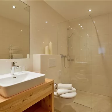 A modern bathroom with a shower and a wooden sink. The walls are light tiled and there are fresh towels.