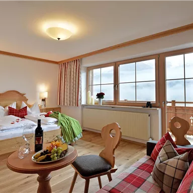 A cozy hotel room with a double bed and a seating area. Large windows provide plenty of daylight and a view of the mountains.