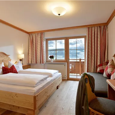 A cozy hotel room with two beds and wooden furniture. Large windows offer a view outside, decorative cushions and fruits on the table create an inviting atmosphere.