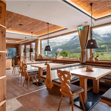 Ein gemütliches Restaurant mit Holzinterieur und großen Fenstern. Der Blick auf die Berge und die Weinregale sorgen für eine einladende Atmosphäre.