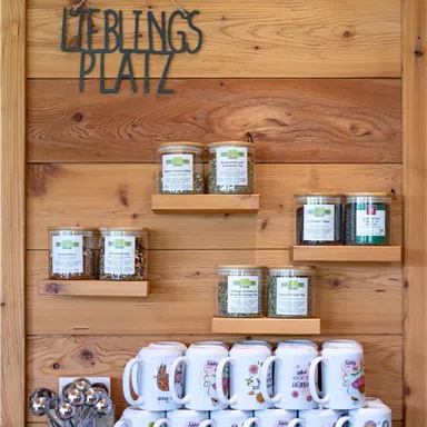 Ein schöner Holzregal mit verschiedenen Gläsern und Tassen. Darüber hängt ein Schild mit der Aufschrift „Lieblingsplatz“.