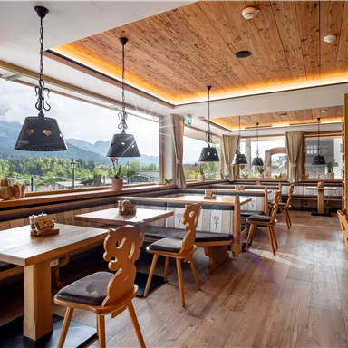 Ein modernes Restaurant mit Holzmöbeln und großen Fenstern, die einen Blick auf die Berge bieten. Die Einrichtung ist gemütlich und einladend.