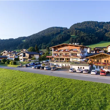 Ein ruhiges Dorf in den Bergen mit traditionellen Holzgebäuden. Die Landschaft ist grün und die Sonne scheint.