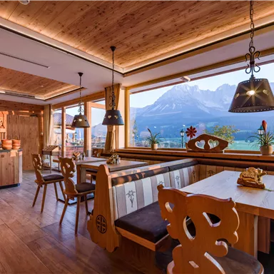Ein gemütliches Restaurant mit Holzinterieur und großen Fenstern. Im Hintergrund sind beeindruckende Berglandschaften zu sehen.